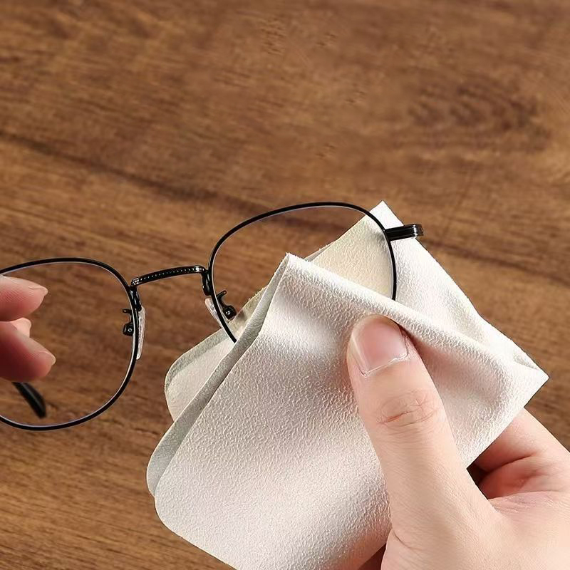 Hand using microfiber cloth to clean glasses lens on wooden table