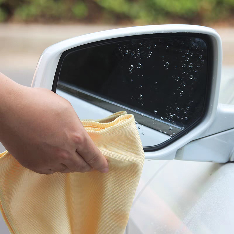 Microfiber cloth used on side mirror of car to remove water droplets